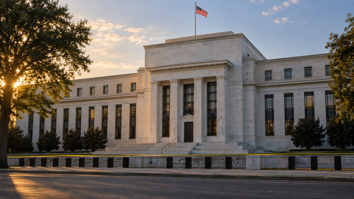 Neoclassical central-bank style stone building seen across a quiet street with a small United States flag